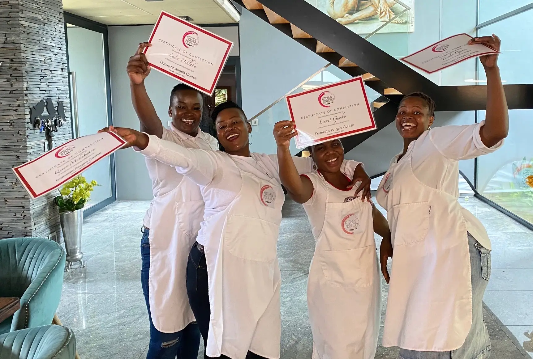 Four Kitchen Addiction short course graduates in aprons celebrating with their certificates of completion